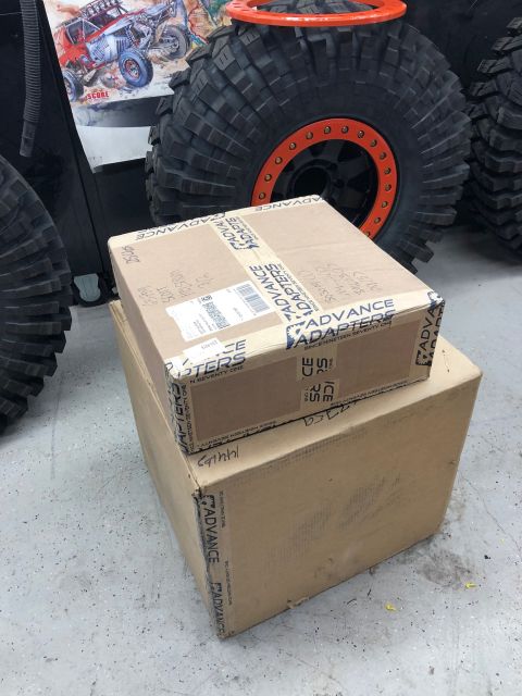1992 Jeep Wrangler - Cardboard boxes from Advance Adapters sit near large off-road tires and a graphic of a buggy.
