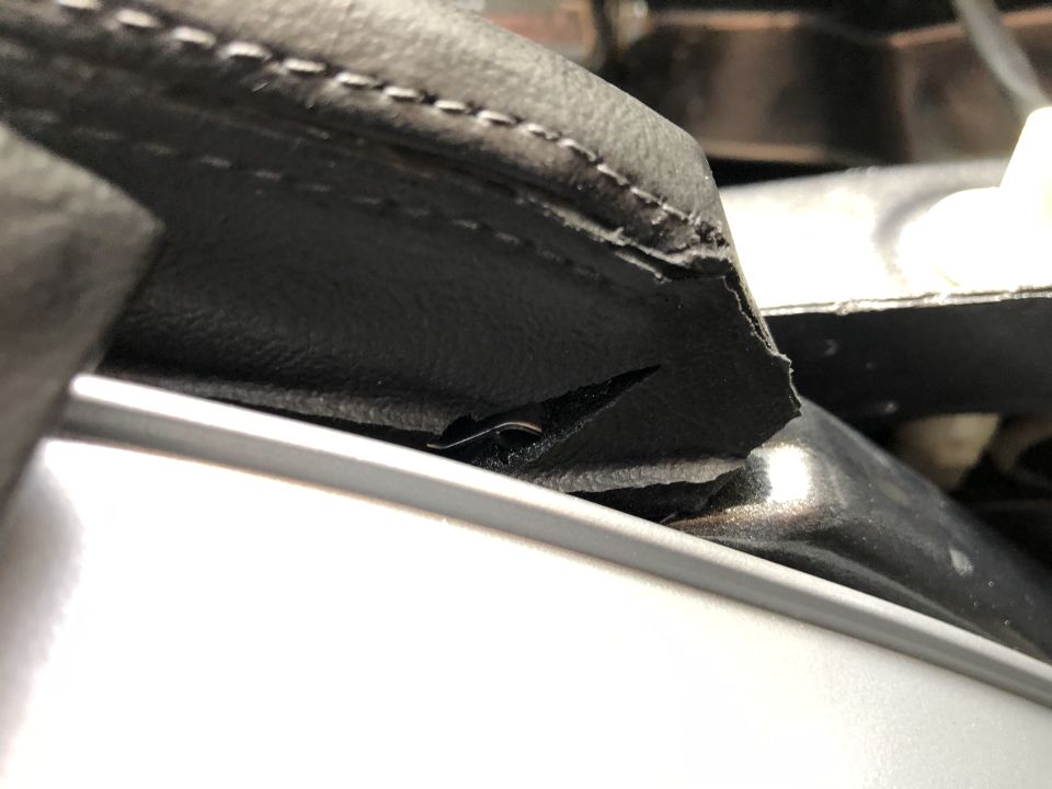 Close-up of torn black vinyl trim inside a car, showing stitching and a ripped edge