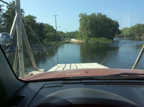 1992 Ford Bronco - View from inside a vehicle on a ferry crossing a wide, calm body of water with lush green trees on the banks.