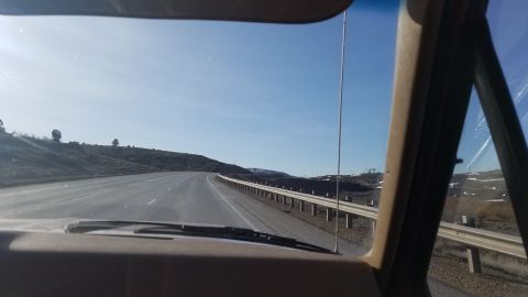 1985 Ford Bronco - View from inside a vehicle on a highway, with rolling hills and a guardrail visible.