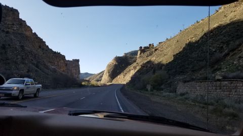 1985 Ford Bronco - Pickup truck travels through a scenic canyon on a sunny day.