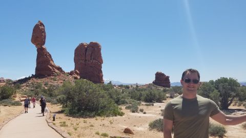1985 Ford Bronco - A man stands in front of iconic rock formations at Arches National Park under a clear blue sky.