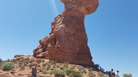 1985 Ford Bronco - A person stands in a desert landscape with a prominent sandstone rock formation under a clear blue sky.