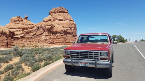 1985 Ford Bronco - This 1985 Ford Bronco is parked on a road in a desert landscape with distinctive red rock formations under a clear blue sky.
