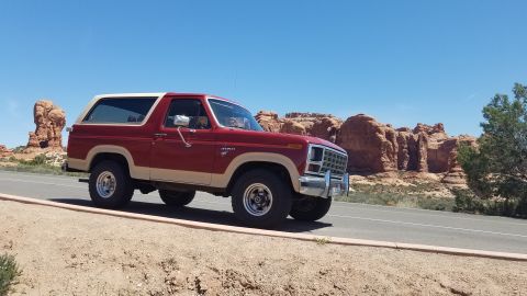 1985 Ford Bronco - A two-tone Ford Bronco navigates a desert landscape under a clear blue sky.