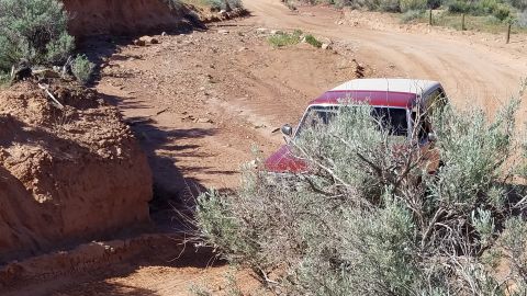 1985 Ford Bronco - A vintage SUV drives through a dry, desert landscape on a rough dirt track.