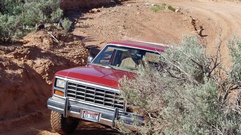 1985 Ford Bronco - 1985 Ford Bronco navigating a dusty, off-road trail with sparse vegetation.