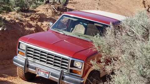 1985 Ford Bronco - This red SUV is navigating a rough dirt path, with its front end angled towards the viewer.