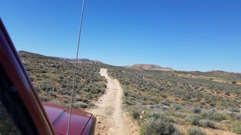 1985 Ford Bronco - A red SUV navigates a dusty trail through a sparse desert landscape on a clear day.