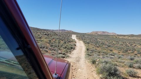 1985 Ford Bronco - Driving a red SUV on a remote dirt road through a desert landscape with sparse vegetation.