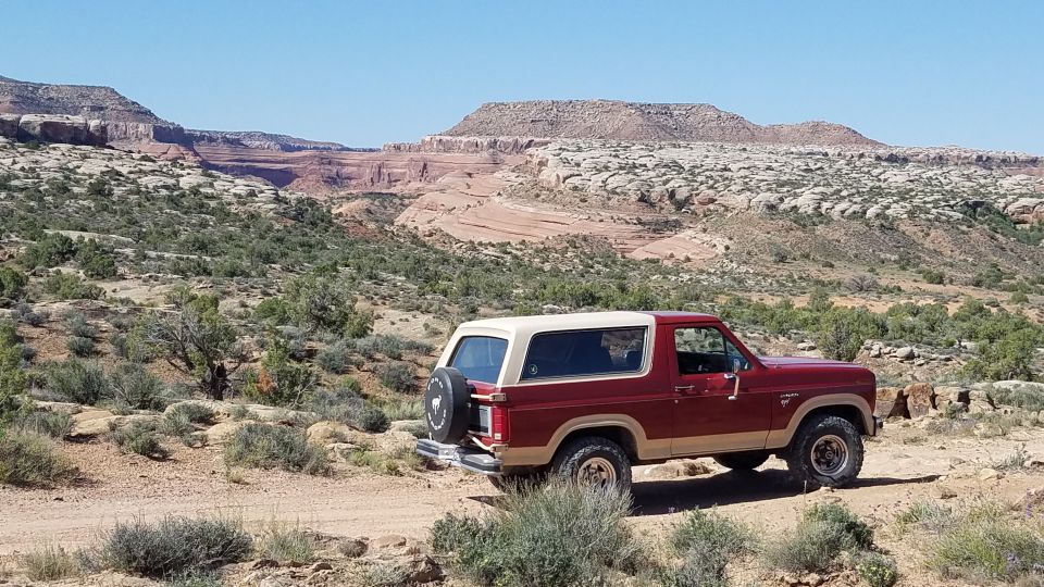 Red 1985 Ford Bronco parked on dirt road in desert with red rock formations in background
