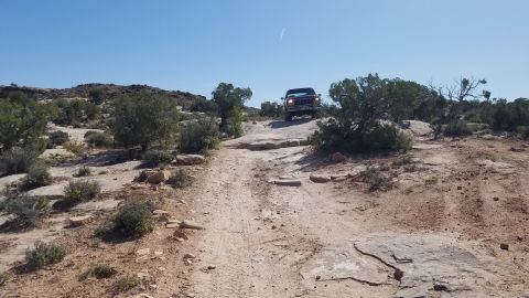 1985 Ford Bronco - A Ford Bronco navigates a challenging off-road path in a desert landscape.