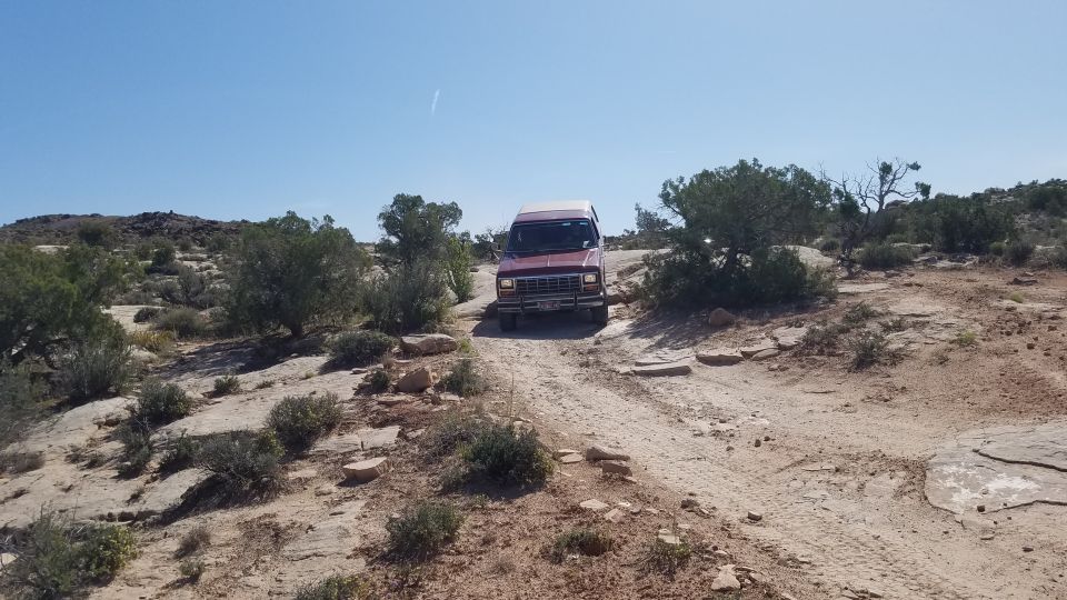 Red van with a prominent grille driving on a dirt road in a desert landscape
