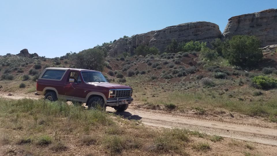 Maroon Ford Bronco driving on a dirt road in a desert landscape with rocky hills