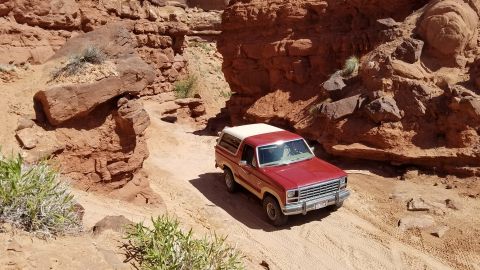 1985 Ford Bronco - This SUV navigates a narrow dirt path through a rocky canyon landscape.