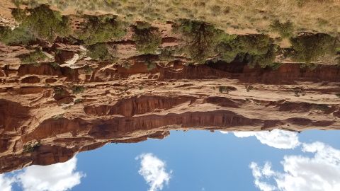 1985 Ford Bronco - A vast desert landscape unfolds with towering red rock cliffs under a bright blue sky dotted with white clouds.