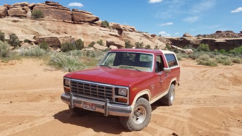 1985 Ford Bronco - 1985 Ford Bronco parked in a desert landscape with red rock formations.