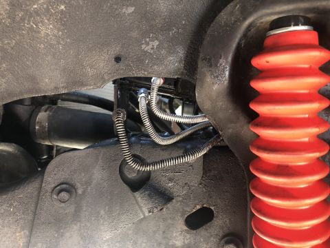 1995 Ford Bronco - A close-up view of the suspension components of a vehicle, showing a red shock absorber boot and braided metal brake lines.