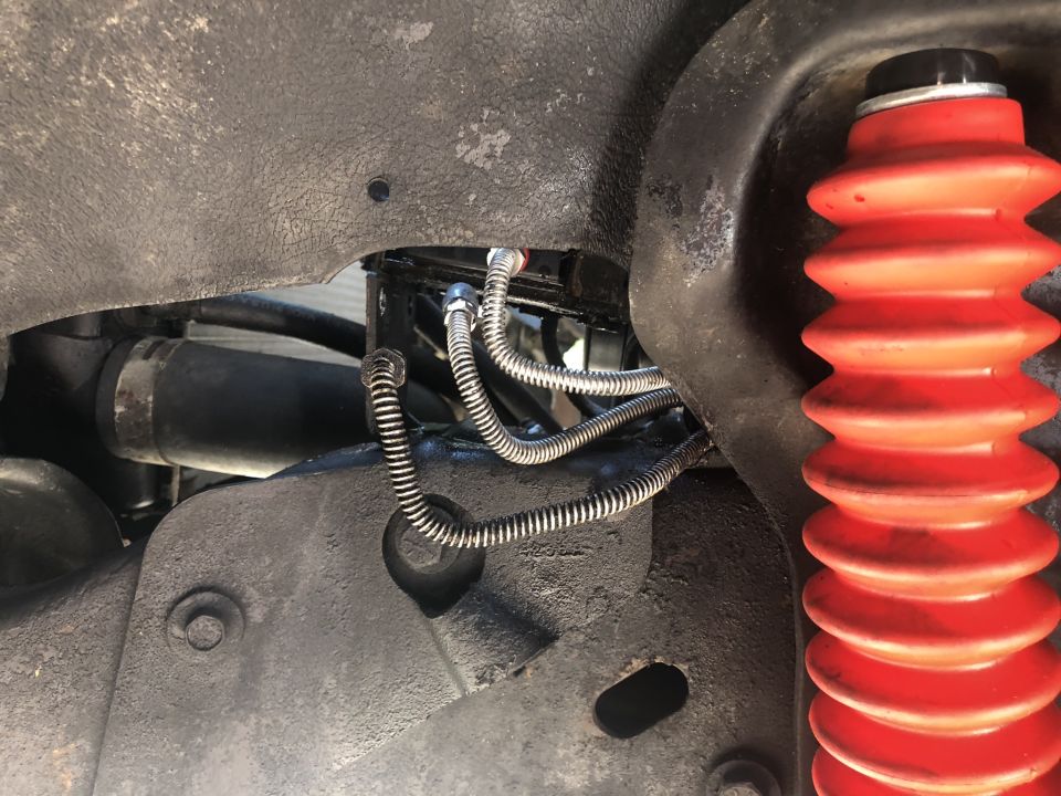 Close-up of vehicle suspension with red shock boot and brake lines.