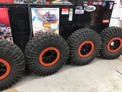 1992 Jeep Wrangler - Four large off-road tires with black rims and orange beadlocks are displayed in front of a black toolbox with various stickers and posters.…