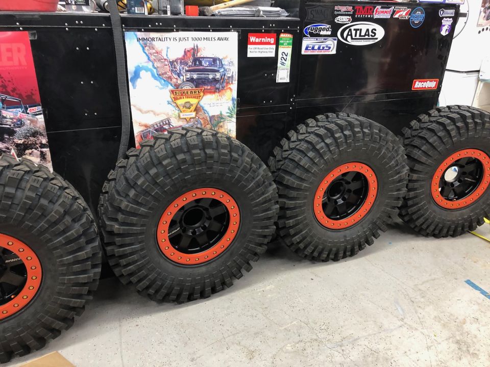 Four large off-road tires with black rims and orange beadlocks in front of a toolbox.