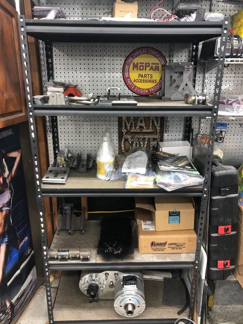 1992 Jeep Wrangler - A metal shelving unit is filled with various automotive parts and accessories. Visible items include a Mopar sign, boxes, and a large mecha…