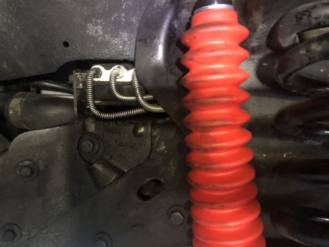 1995 Ford Bronco - A close-up view of the suspension components on a vehicle, featuring a red bellows boot and a black coil spring. A metal bracket with coile…