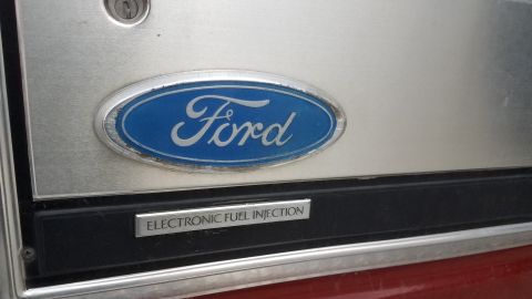 1985 Ford Bronco - A close-up of a Ford emblem on a brushed metal surface, below which is a black panel with the text "ELECTRONIC FUEL INJECTION".