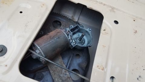 1985 Ford Bronco - A close-up view of a rusty power window motor assembly and its associated gear mechanism, mounted inside the door frame of an older vehicle.