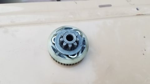 1985 Ford Bronco - A close-up, overhead view of a starter drive gear assembly with a 10-tooth pinion gear. The assembly has a white plastic housing with metal…