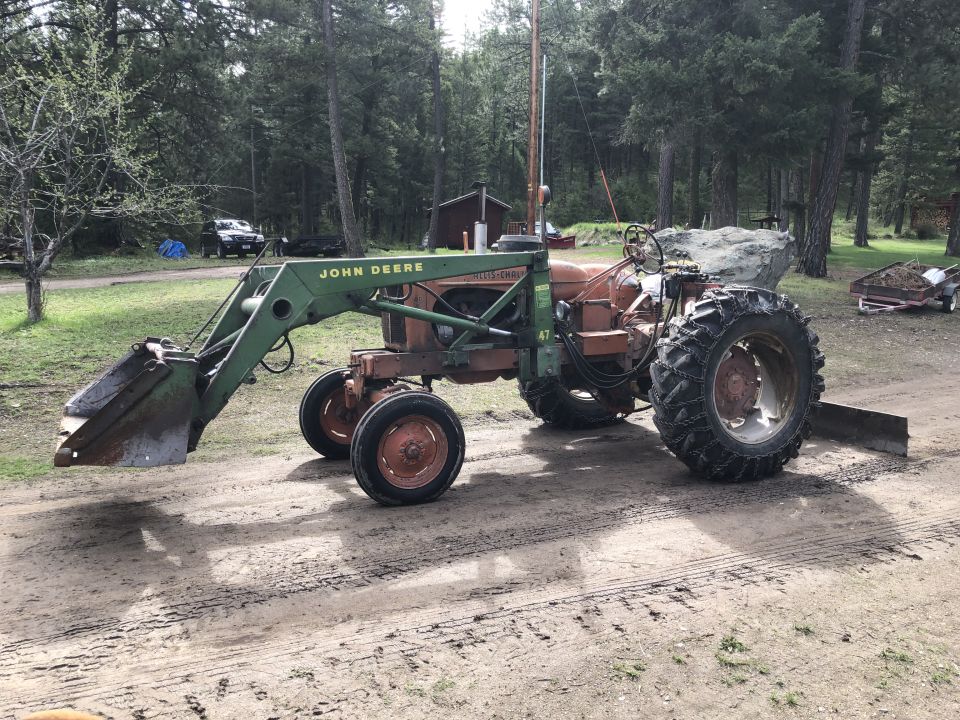 Vintage orange and green tractor with front loader and rear blade, parked on dirt path.
