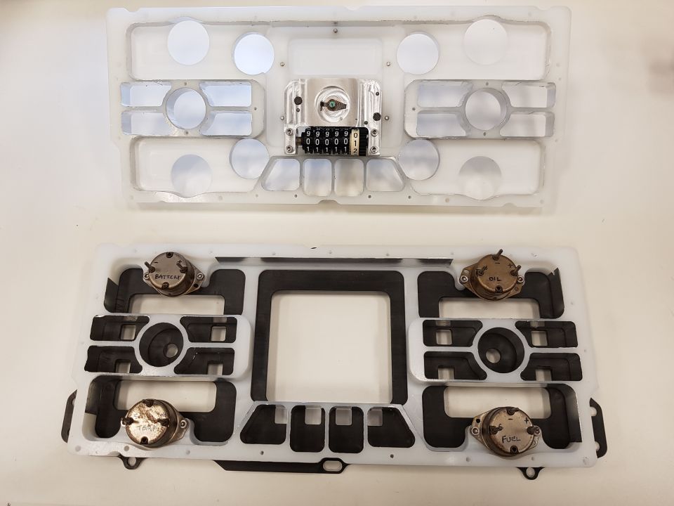 Two parts of a dashboard instrument cluster, one with a odometer and gauge mounts, the other with fuel and oil sending units