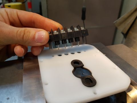1978 Ford Bronco - A hand holds an electrical terminal block above a white plastic part with mounting holes and a rubber grommet.