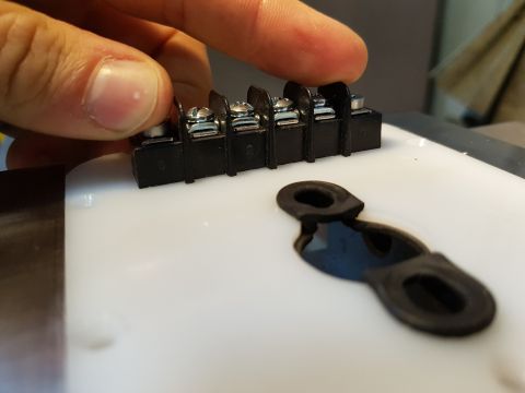 1978 Ford Bronco - Close-up of a terminal block and rubber grommets, with a finger pressing down on the block.
