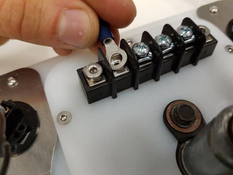 1978 Ford Bronco - A hand connects a blue-capped wire to a black terminal block, part of a vehicle's electrical system.