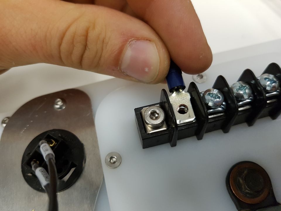 Hand connecting a blue wire terminal to a black screw terminal block