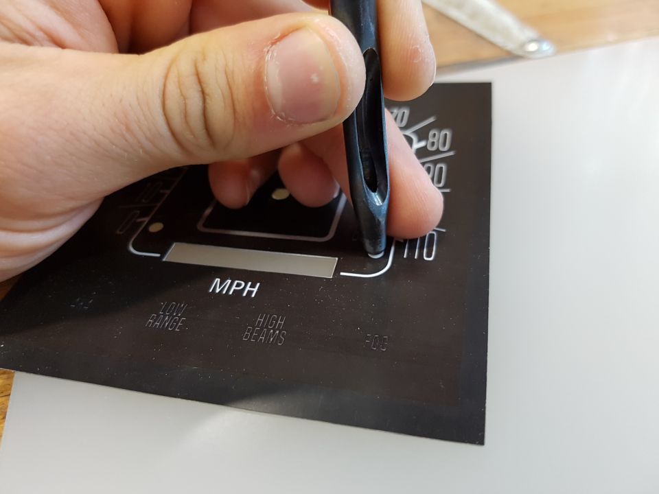 Close-up of a hand holding a punch tool over a black gauge face with white text.