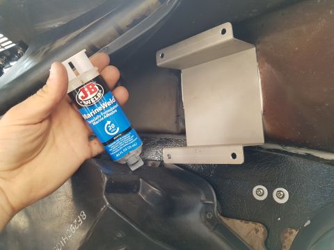 1978 Ford Bronco - A hand holds a tube of JB Weld MarineWeld adhesive next to a silver metal bracket mounted inside a vehicle.