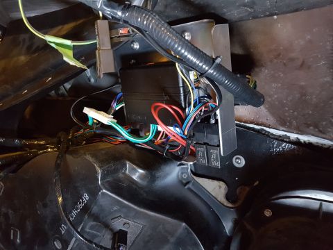 1978 Ford Bronco - A close-up view shows a black aftermarket electronic control module with numerous colorful wires connected to it, mounted behind a plastic…