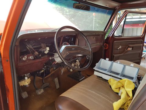 1978 Ford Bronco - The interior of a classic Ford truck or SUV is shown, with the dashboard disassembled. A steering wheel, pedals, and wiring are visible, al…