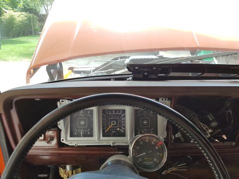 1978 Ford Bronco - The interior of a vehicle dashboard is shown, featuring a steering wheel, instrument cluster with gauges, and an open hood in the backgroun…