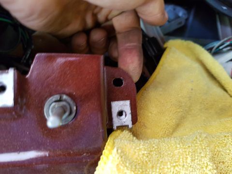 1978 Ford Bronco - A hand is shown manipulating a red metallic bracket with a bolt and nut assembly. A yellow cloth is visible to the right, partially obscuri…
