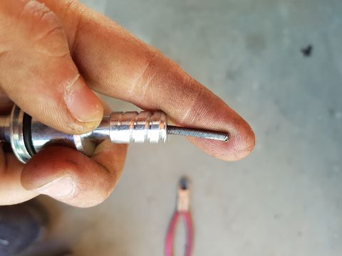 1978 Ford Bronco - A person's hand is holding a metal threaded rod with a spring-like coil. The background is a concrete surface with a pair of pliers out of…