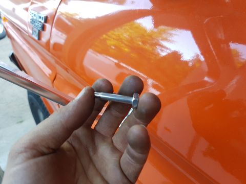 1978 Ford Bronco - Close-up of a bolt being held near the fender badge of a 1978 Ford Bronco.