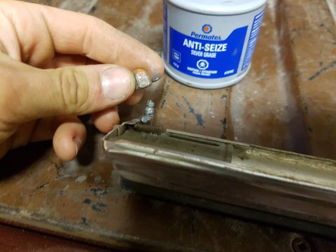 1978 Ford Bronco - A hand holds a screw and a metal trim piece, with a can of anti-seize visible, suggesting a repair or maintenance task.