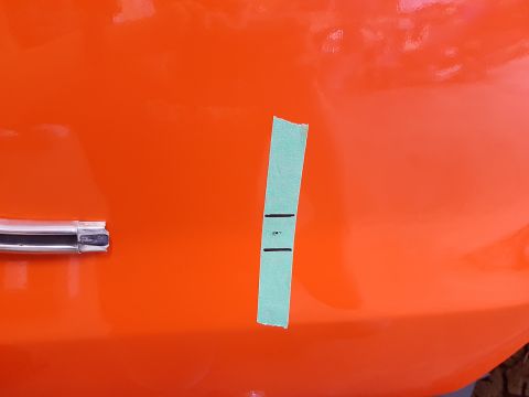 1978 Ford Bronco - A piece of tape with markings is applied to an orange vehicle panel.