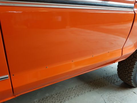 1978 Ford Bronco - Close-up of an orange vehicle's side panel, showing the door seam and a portion of the tire.