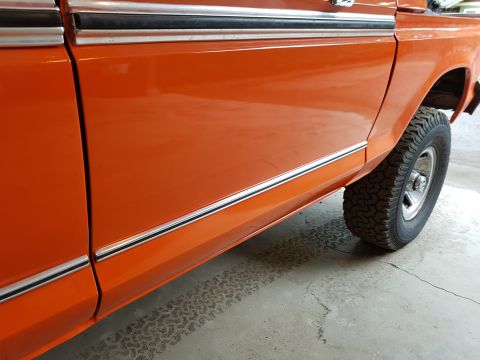 1978 Ford Bronco - The side profile of an orange 1978 Ford Bronco shows its distinctive body lines and a knobby off-road tire.