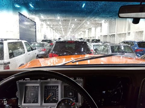 1978 Ford Bronco - View from inside a vehicle, looking through a wet windshield at other cars parked in a lot.