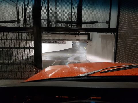 1978 Ford Bronco - View from inside an orange vehicle as it approaches a parking garage with a clearance sign overhead.